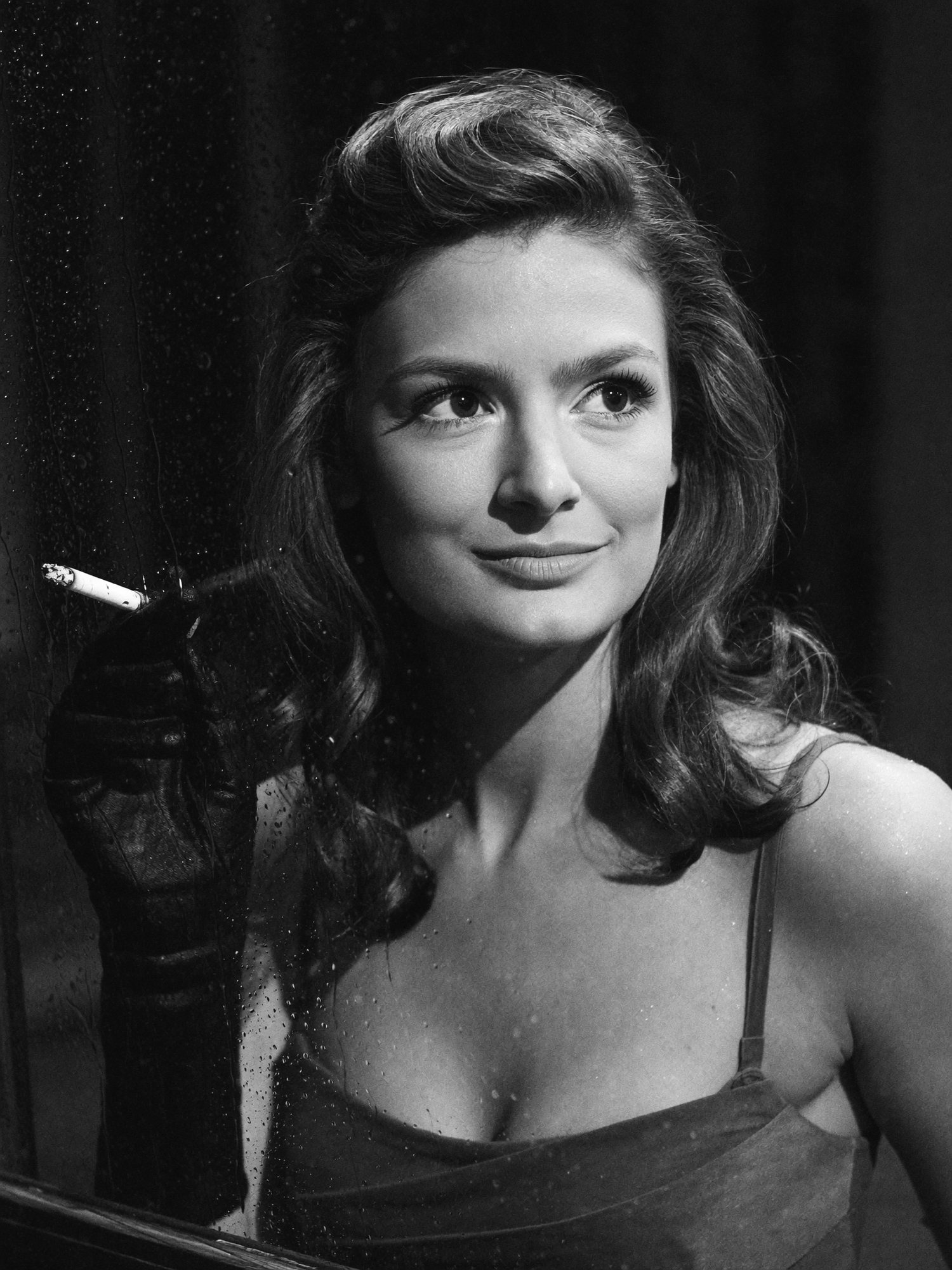 Carla with a cigarette behind a rain-streaked window. Black and white.