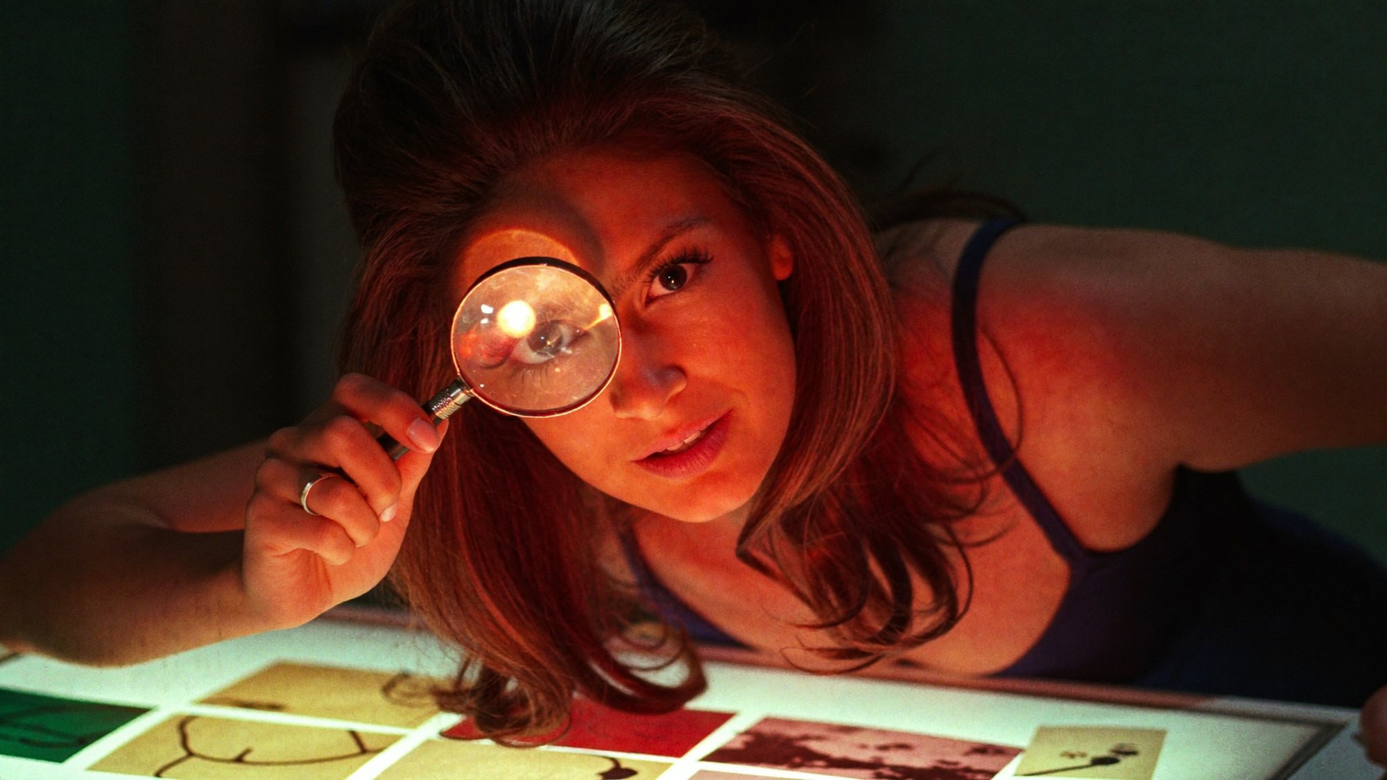 Carla studying a contact sheet on a light box through a magnifying loupe, lit red from below.
