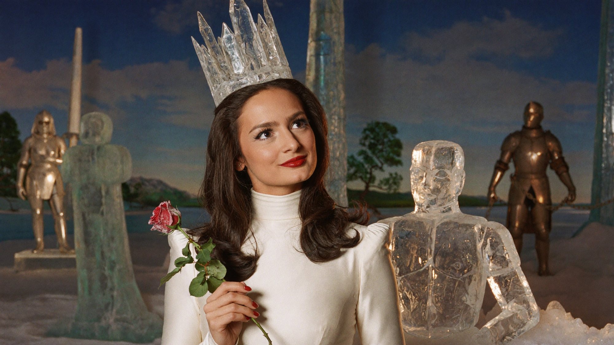 Carla as an ice queen in a crystal crown and white high-necked gown, holding a red rose among ice-sculpture knights.