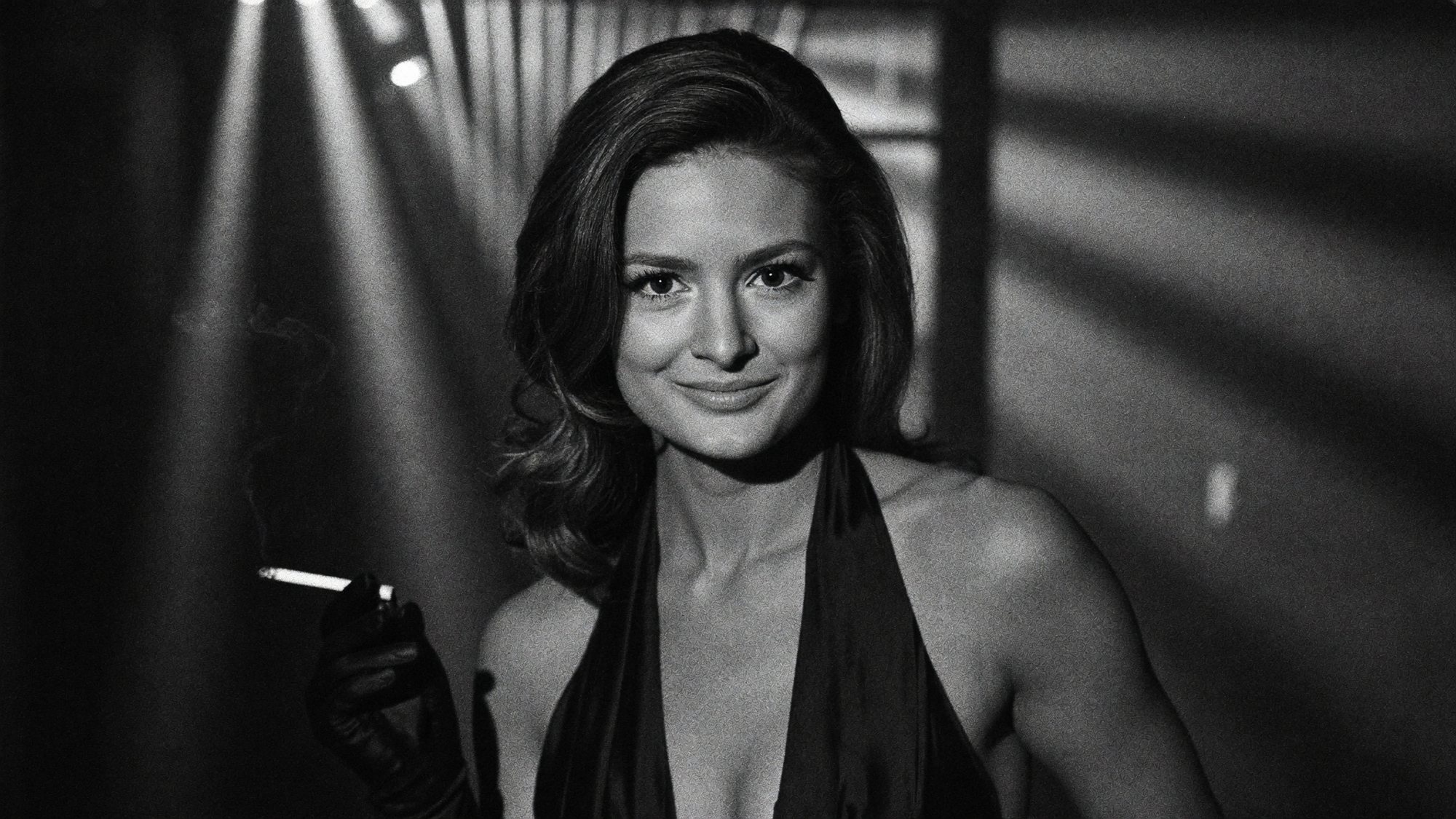 Carla in black and white holding a cigarette in slatted spotlight beams.